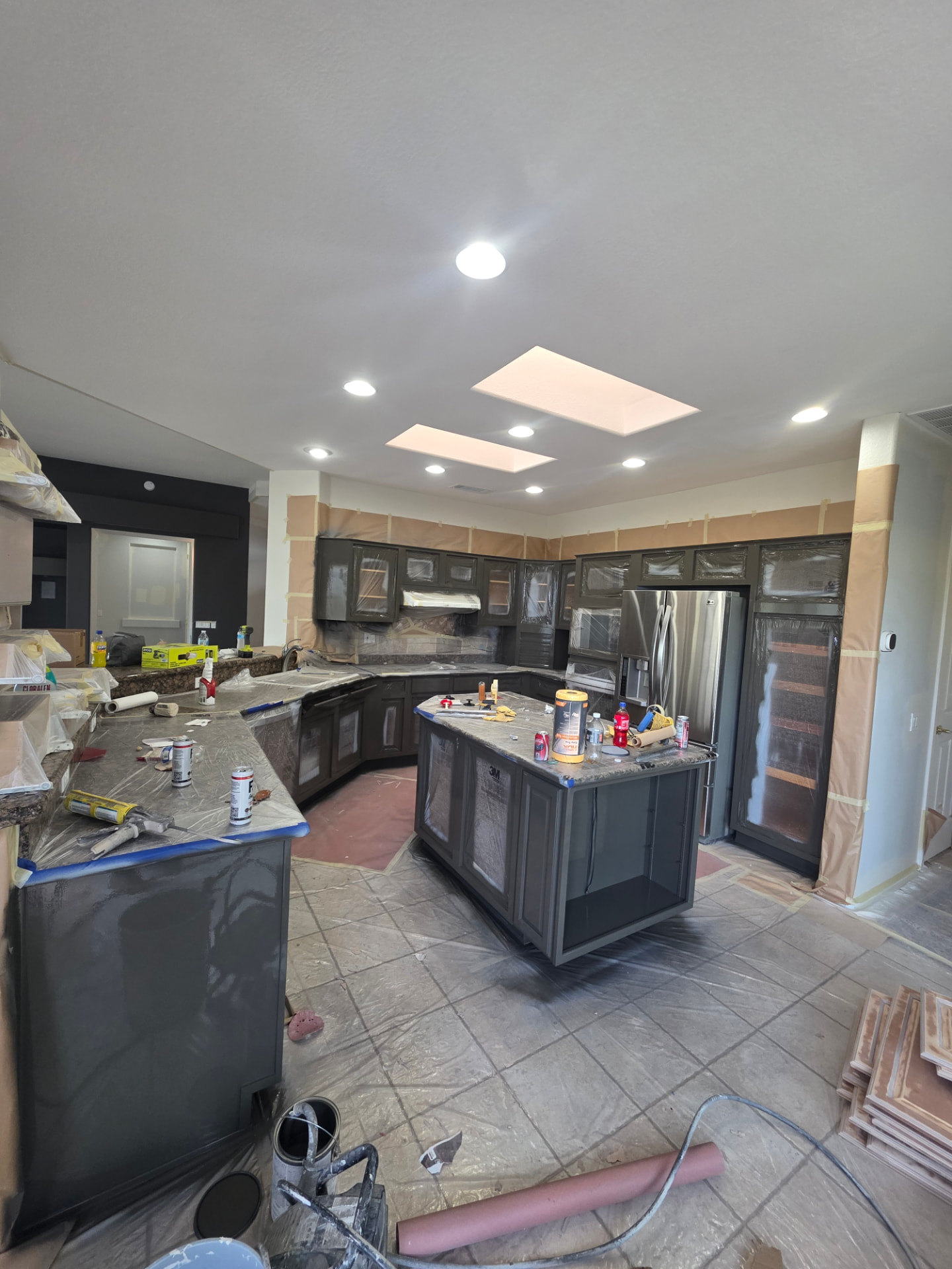 Kitchen cabinets painted dark with counters and floors covered in protective plastic